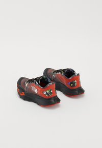 Chaussures de sport rouges et noires avec une tige en maille texturée, des accents floraux et une épaisse semelle en caoutchouc noir. Comprend des détails de marque et des lacets.