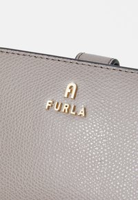 Gray textured leather bag with gold logo "FURLA" and visible stitching details. Compact design, smooth finish, and distinctive shape.
