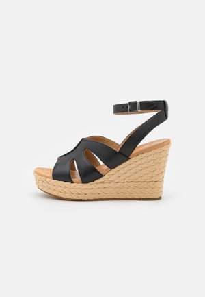Sort læder kilehæl sandal med ankelrem og spænde, med udskåret overdel og tan fletplatform hæl.