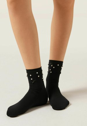 Sorte sokker lavet af glat stof, med dekorative elementer som små perler og sløjfer ved anklen. Klassisk, tætsiddende form.