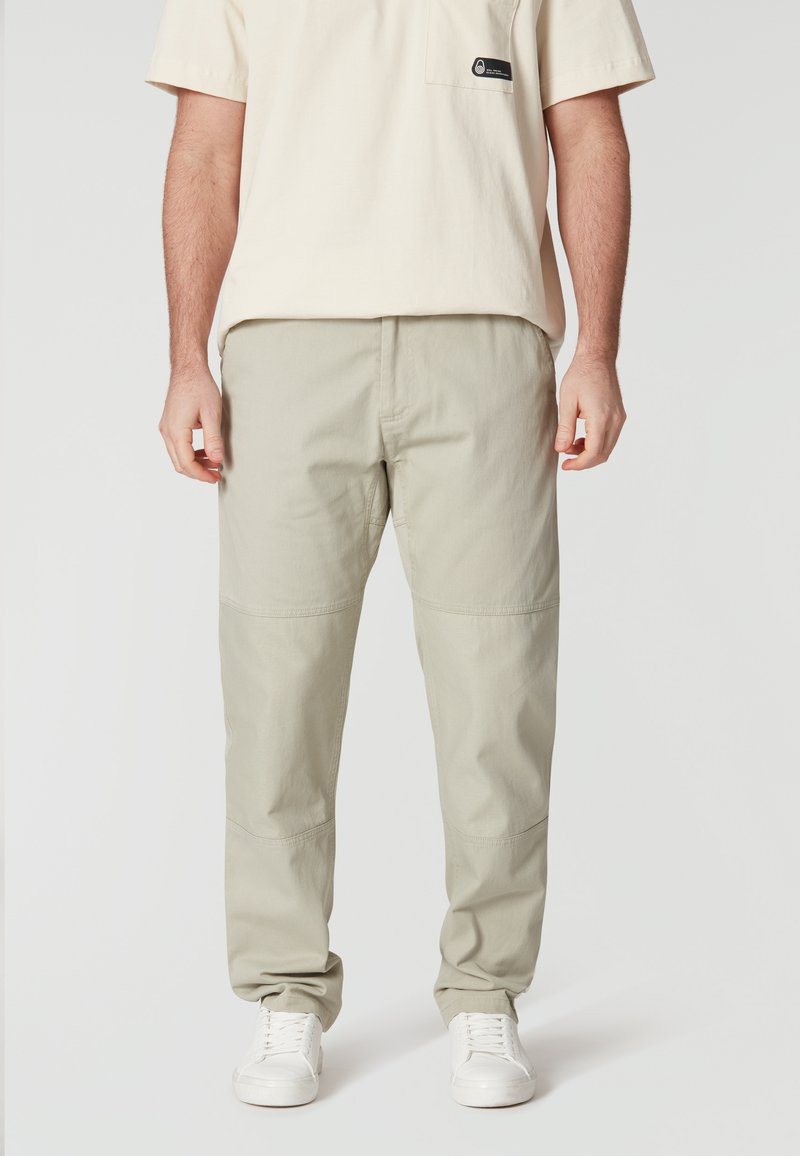 Lichtgroene katoenen broeken in een rechte snit, met knie-patches en subtiele naaddetails, gecombineerd met witte sneakers en een beige shirt.