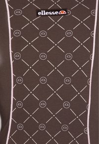 Brązowy t-shirt z tkaniny z geometrycznym wzorem białych linii i kółek, z małym czarnym i kolorowym logo na środku u góry.