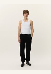 Top sin mangas blanco con pantalones deportivos negros que presentan un parche de logo, corte recto, cinturilla elástica y zapatos negros. Un atuendo simple y casual.