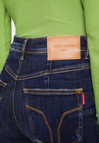 Mörkblå denimjeans med kontrasterande orange sömmar, med en tan läderetikett med "MISS SIXTY" präglat på baksidan.
