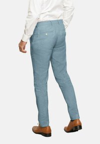 Pantalones de lino azul claro con corte ajustado y dos bolsillos traseros. Combinados con zapatos de cuero marrón y una camisa de vestir blanca.