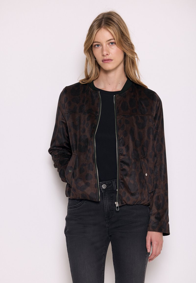 Giacca bomber con stampa leopardata marrone, chiusura con zip, colletto a costine verde e due tasche laterali; indossata sopra una maglietta nera e jeans.