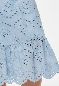 Gaiši zila kokvilnas kleita ar izšūtām acs rakstiem, ar viļņainu apakšmali un izplestu dizainu ar teksturālo detaļu.