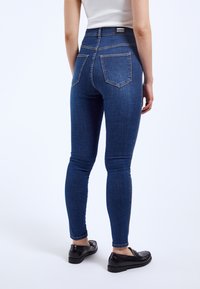 Tmavě modré skinny džíny s vysokým pasem, vyrobené z denimu. Obsahují dvě zadní kapsy a kontrastní švy. V kombinaci s černými mokasíny.