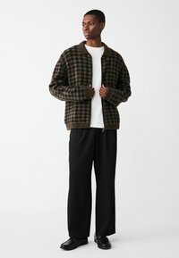 Brūnā rūtainā jaka ar stāvošu apkakli, uzvilkta virs baltas krekla. Iespējas ar elastīgām piedurknēm un brīvu piegriezumu. Stilizēta ar melnām biksēm un apaviem.