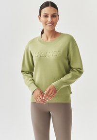 Sudadera verde clara con cuello de canalé, que presenta un diseño en relieve de "BALANCE" en la parte frontal. Manga larga y corte relajado.