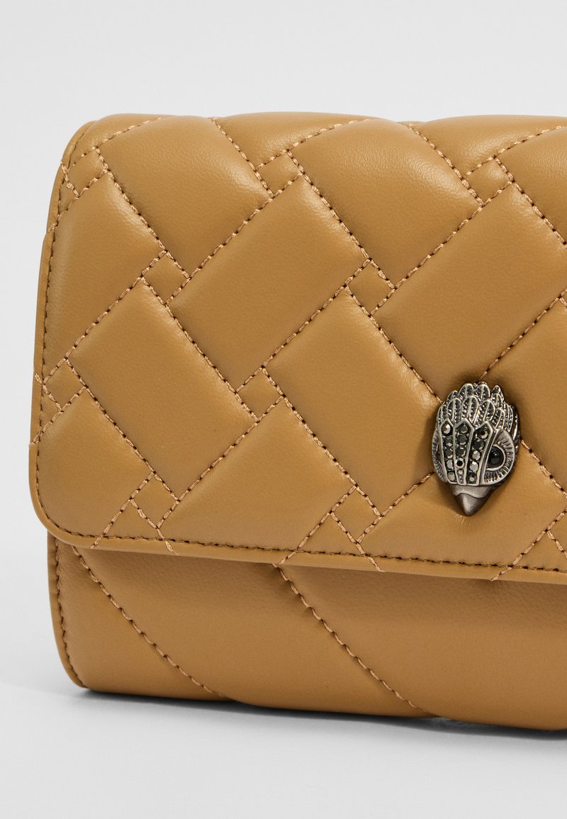 Portefeuille en cuir matelassé tan avec une forme structurée, ornée d'un accent en métal argenté décoratif sur le devant et de détails de couture contrastés.