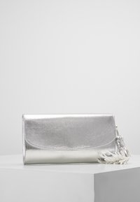 Metallic sølv clutch med en glat tekstur, rund flaplukning og en dekorativ frynseaccent. Kompakt design, egnet til formelle anledninger.