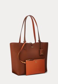 Brun teksturert skinnveske med to lange håndtak og en festet oransje håndleddveske med gullfargede initialer.