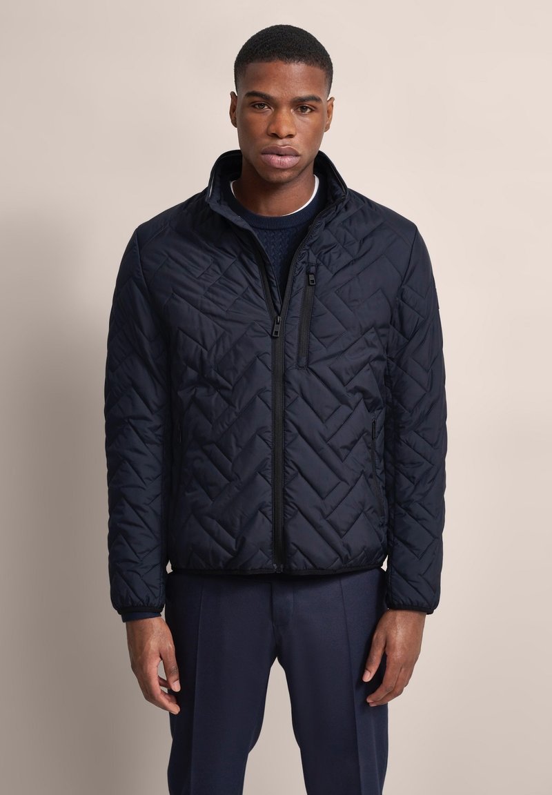 Marineblau gesteppte Jacke mit hohem Kragen, ausgestattet mit einem Reißverschluss und strukturiertem Muster. Mit seitlichen Taschen für zusätzliche Funktionalität gestaltet.