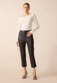 White ribbed long-sleeve top paired with high-waisted black leather pants. Model wears black strappy heels. Smooth textures and fitted design.