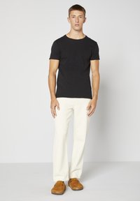 Černé tričko s krátkým rukávem a kulatým výstřihem, v kombinaci s krémovými kalhotami širokého střihu a hnědými semišovými botami. Jednoduchý a moderní design.