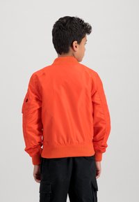 Orange bomber jacket with ribbed cuffs and hem, featuring a smooth texture and a side pocket. Worn by a child facing away from the camera.