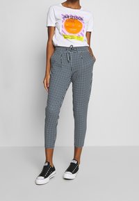 Czarno-białe spodnie w kratę o zwężanym kroju, z elastycznym pasem i wiązaniem, połączone z graficznym białym t-shirtem i czarnymi trampkami.