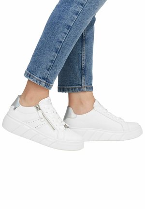 Baskets blanches à lacets avec une semelle texturée, accent argenté au niveau du talon et détail zippé sur le côté. Jean en denim à longueur de cheville visible.