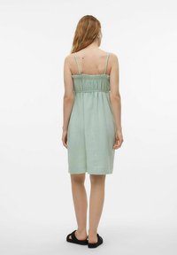 Jasnozielona sukienka do kolan na cienkich ramiączkach, ze zgromadzonym w talii materiałem i teksturowanym wykończeniem. Posiada falbaniasty dekolt i gładki dół.