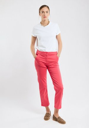 Pantalons roses ajustés avec fermeture à bouton et poches, associés à un t-shirt blanc à manches courtes et des chaussures à imprimé léopard marron.