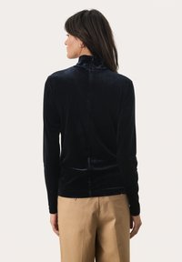 Navyblaues Samt-Turtleneck-Oberteil mit langen Ärmeln und hohem Kragen, mit einer mittigen Naht auf der Rückseite, kombiniert mit beigen Hosen.