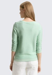 Mintgroene sweatshirt met een gestructureerd geribbeld ontwerp, aangesloten boorden en een zacht afgeronde halslijn, gecombineerd met een witte broek.