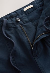 Temno modre široke hlače z zadrgo, gumbnim zapiranjem, vrvico za zategovanje in vidnimi šivi. Mehka tkanina z gladko teksturo.