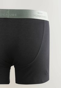 Schwarze Baumwollboxershorts mit einem hellgrünen, gebrandeten Bund. Sie haben eine glatte Textur und gerade Nähte entlang der Kanten.