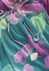 Bloemenprintstof met grote roze en groene bloemen op een teal achtergrond, gemaakt van lichtgewicht, doorschijnend, vloeiend materiaal met strikdetail.