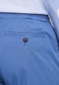 Pantaloni blu realizzati in tessuto leggero, dotati di vita elastica, una tasca piatta con un bottone nero e una texture sottile.