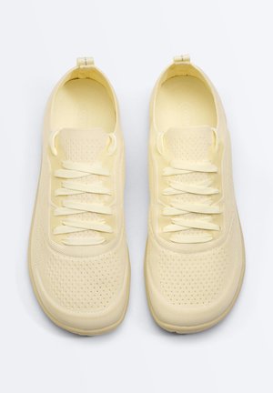 Pair of light yellow knitted fabric sneakers with matching laces, perforated upper, and pull tabs on back.