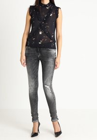 Sleeveless black floral blouse with ruffles paired with distressed gray skinny jeans and black high heels on a neutral background.