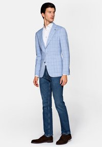 Jasnoniebieska marynarka w kratę z lekkiego materiału, z klapami typu notch, zapinana na pojedynczy guzik, w połączeniu z ciemnoniebieskimi dżinsami i brązowymi butami.
