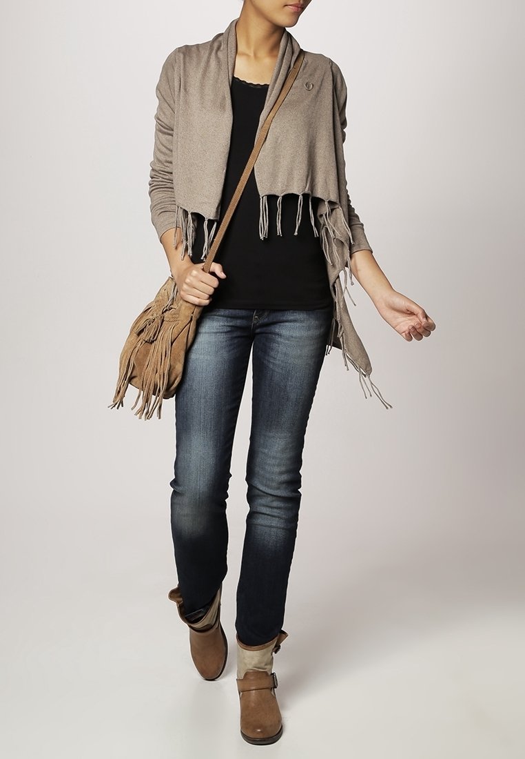 Wrap in khaki con frange, top nero, jeans slim in denim, stivaletti marroni alla caviglia. Materiale morbido, vestibilità rilassata, borsa testurizzata e leggeri dettagli drappeggiati.
