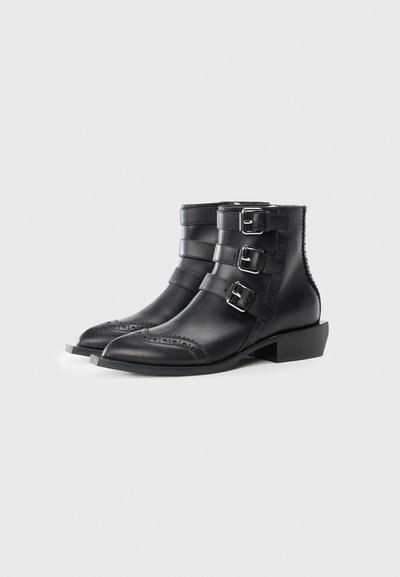 Stivaletti neri in pelle con tre fibbie metalliche e dettagli in brogue. Presentano una punta appuntita e un tacco basso a blocco.