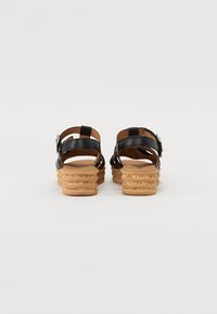 Des sandales en cuir noir avec des talons en liège multi-couches. Elles disposent de brides ajustables au niveau de la cheville et d'un intérieur lisse.