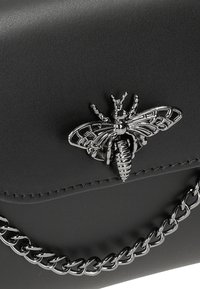 Borsa a mano in pelle nera con un'ornamentazione a forma di ape metallica e una tracolla in catena argentata. Texture liscia con dettagli in hardware a contrasto.