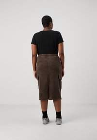 Top scurt negru cu mânecă scurtă, asortat cu o fustă cargo maro, lungime până la genunchi, cu talie elastică și buzunare laterale. Adidași argintii și șosete negre.