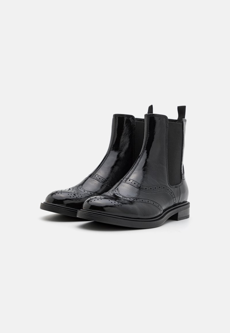 Des bottes Chelsea en cuir verni noir présentent un bout arrondi, des panneaux latéraux élastiques, des détails décoratifs en brogue et un petit talon empilé.