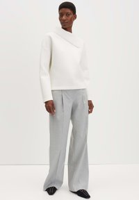 Maglione bianco corto con un colletto a coste asimmetrico, abbinato a pantaloni palazzo grigi chiari a vita alta e scarpe nere a punta.