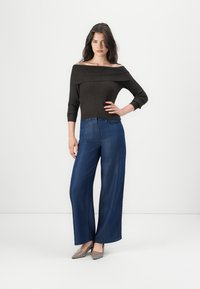 Dark ribbed off-shoulder top paired with wide-leg blue denim jeans. The outfit is complemented by light gray heels. Simple, modern design.