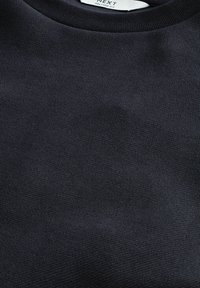 Tmavě námořnický svetr vyrobený z texturované tkaniny s kulatým výstřihem a žebrovanými manžetami. Na vnitřní straně se nachází štítek s označením 'NEXT Relaxed Fit.'