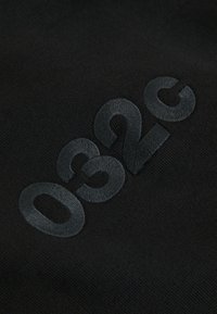 Gros plan sur un tissu noir avec un logo "032c" brodé en relief avec un fil noir assorti.