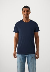 Marineblå bomullst-skjorte med rund hals og korte ermer, som har en glatt tekstur og en vanlig pasform. Brukt med lyseblå jeans.