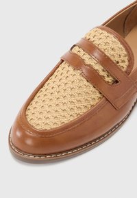 Pruunid nahast loafersid, mille pealmine on kootud beezis, sisaldavad kaht rihma üle jala ja ümarat varvast, detailne tikand taldadel.