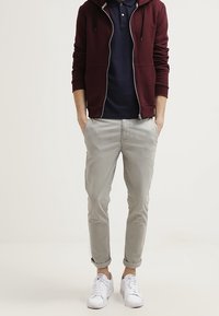 Burgundowy polar zapinany na zamek w połączeniu z granatowym polo, zestawiony z jasnoszarymi spodniami chinos w rolowanych kostkach i białymi trampkami. Prosty, casualowy styl.