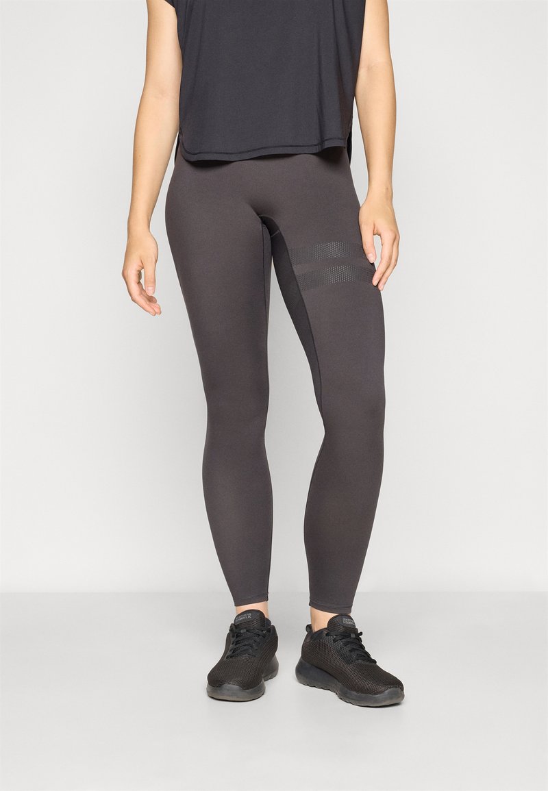 Dark gray leggings made from stretchy material, fitted design, featuring textured side panels and paired with a loose black top and black shoes.