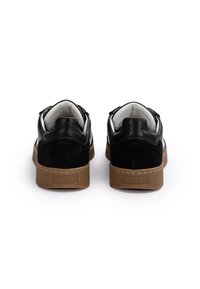 Coppia di sneakers bianche e nere con suole marroni viste da dietro su sfondo bianco, nome del marchio "LLOYD" sulla suola.