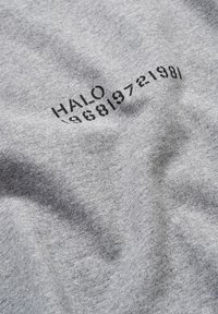 Grå bomullstyg med en slät textur, med tryckt svart text "HALO 19681972198/" i en böjd layout.